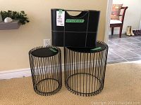 Two black metal wire round end tables and one black magazine rack against a beige wall and carpet.