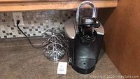 Keurig coffee maker and metal coffee pod rack on kitchen counter.