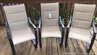 Three beige sling patio chairs on wooden deck, front view