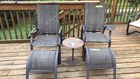 Wide view of the 2 patio chairs with their foot stools and small round metal table on wooden deck