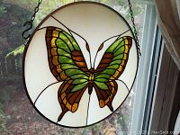 Circular stained glass featuring green and brown butterfly with yellow accents on white background