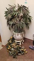 Full view of artificial tree in ceramic pot on stand along with two artificial garlands on floor