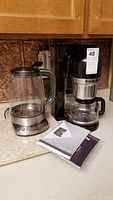 KitchenAid coffee maker with glass carafe and Breville multi-temp kettle side by side on counter, with instruction manuals in front