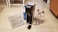 Front view of SodaStream Source model, CO2 cartridge, bottles, and shelf riser on floor.
