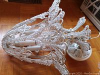 Side view of chandelier frame showing off-white speckled metal scroll arms with attached clear glass bead strands