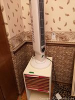 Side view of Lasko oscillating tower fan positioned on composite shelf unit with visible Letraset boxes in shelf opening.