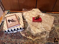 Overview photo showing artificial silk mat, decorative box, notebook, and lace textiles stacked on carpeted floor.