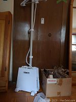 Full view of Conair Extreme Steam fabric steamer with adjustable stand next to a box filled with clear plastic hangers.