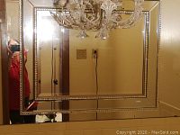 Full view of the rectangular beveled wall mirror showing its beveled inner mirror and decorative beveled border reflecting a chandelier and room.