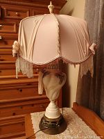Front view of the pink fabric boudoir lamp with ceramic floral base and bronze-tone footed base on a wooden table