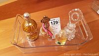 Four perfume and scent bottles displayed in a clear tray, showing decorative details.
