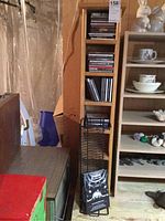 Wooden shelf with 36 CDs stacked in three sections and metal CD rack with additional CDs leaning against the shelf.