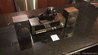Full stereo set on black countertop: main cassette unit with wood sides and silver front, headphones resting on top, two speakers flanking main unit.