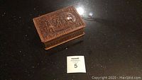 Photo of the full wooden leather covered box with embossed lid design against a shiny black surface, includes lot number card