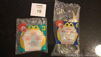 Two McDonalds Kids Meal toys sealed in original bags displayed on floor, one Disney Jasmine Aladdin (#3) and one Baylene Dinosaur (#6), each with Ronald McDonald image and packaging text visible.