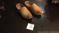 Pair of vintage wooden clogs on a dark surface with auction lot number 22.