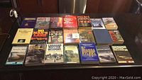 Full view of 23 war-related books arranged on a dark surface with visible titles mainly about weapons and military stories.