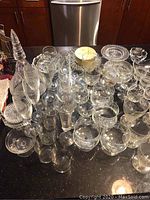 Top view of assorted etched crystal and glass barware including several decanters, wine glasses, and cocktail glasses arranged on a dark countertop.