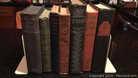 Front view of 7 assorted vintage hardcover books showing condition and titles on spines.