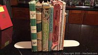 Seven children's books standing upright between two white book ends on a black countertop, showing varying colors and conditions of spines and covers.
