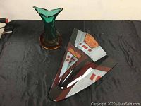 Two art glass vases displayed on a black cloth, one a green and amber 12-inch vase, the other a triangular painted 22.5-inch vase without a stand.