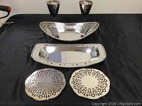 Full lot displayed on black cloth: two goblets, two trays in different shapes, two trivets