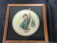 Framed vintage 1971 Hummel plate showing child figure and trees, with 1971 in red, in dark wooden frame.