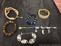 Photo of six vintage costume jewelry bracelets displaying different styles including metallic coil, beads, charm bracelet with glass beads, rhinestone stretch bracelet, and rhinestone oval link bracelet.