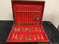 Front view of the open wooden box showing the detailed cutlery pieces neatly arranged in slots with red felt lining.