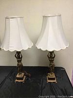 Pair of figural lamps on black table, with off-white fabric shades, approximately 32 inches tall.