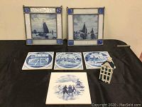 Full lot showing four Blue Delft blue and white ceramic tiles with Dutch scenes, two stained glass hangings with blue sailing ship designs, and a KLM ceramic liquor bottle shaped like a Dutch house