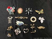 Top view of all 15 costume jewelry brooches displayed on black fabric, showing various designs including floral, animal, cameo, and rhinestone styles.