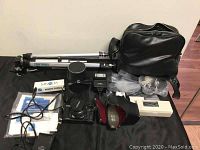 Full overview of camera kit showing Minolta X-700 camera with attached lens, flash unit, remote cord in box, battery charger, black carrying case, lens case, instruction manuals, and Sanwa tripod.