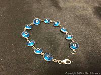 Full view of the 7-inch silver and art glass evil eye bracelet laid flat on a black fabric background.