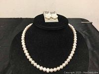 Full view of pearl necklace displayed on black velvet stand with pearl cluster earrings on top.