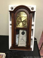 Full view of the Daniel Dakota quartz wall clock in original packaging, showing wooden case with arched top placed inside white styrofoam fitting.