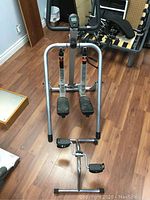 Two pieces of exercise equipment on hardwood floor: a larger walking machine with foot pedals and digital display, and smaller pedal exerciser.