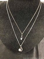 Both necklaces arranged on a black stand, the pearl pendant necklace shorter and the cubic zirconia necklace longer.