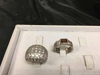 Two sterling silver rings displayed, one with cubic zirconia stones and another with a rectangular garnet stone.