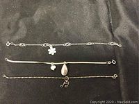 Lot of three sterling silver bracelets laid out on black fabric background showing the entire length and charms