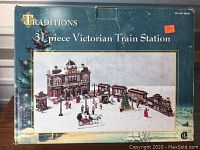 Box front showing the Traditions 31-piece Victorian Train Station set wrapped in blue packaging with image of the assembled village.