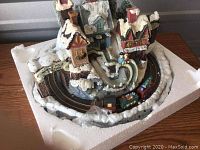 Three-quarter view showing village buildings with snow and lit effects, and small train on track.