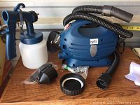 Joined components: motor unit, spray gun, hose, container, nozzles, caps laid out on wood surface