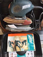 Overview image of Black & Decker Mouse sander polisher along with sandpaper sheets and user guide in a black carrying case.