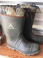 Side view of Kamik boots showing rubber lower with camo fabric upper cuff, laced at top with drawstrings.