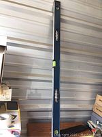 Tall blue 4-foot level vertically positioned against a wall showing three bubble vials and dual hand grips