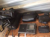 Sony mini camcorder with leather strap and case, Bushnell binoculars case, short wave radio unit on wooden surface