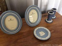 Two blue oval Wedgwood Jasperware picture frames, small round plate with classical white relief profile and leaf border, and a pair of blue Jasperware candle holders with white relief bands on the top and bottom edges. Pieces show wear including scratches and dust.