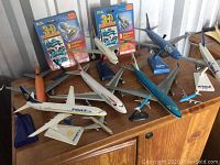 Overview of model airplanes including two in packages and multiple loose models displayed on a wood cabinet, showing Ryanair, ZipAir, and other commercial jets.