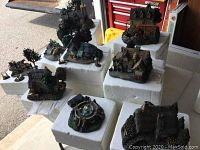 Photo showing multiple Thomas Kinkade sculpted houses and decorative pieces arranged on white foam blocks.